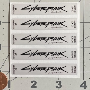 May include: A sheet of rectangular stickers with the word "Cyberpunk" in a stylized font, along with the numbers "2077". Each sticker also has the text "Property of" and "Do Not Remove". The stickers are on a white background.
