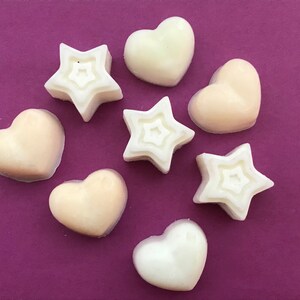 May include: Assortment of white and off-white heart and star shaped wax melts on a purple background.