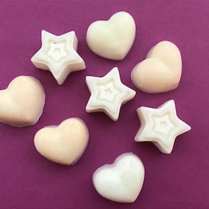May include: Assortment of white and off-white heart and star shaped wax melts on a purple background.