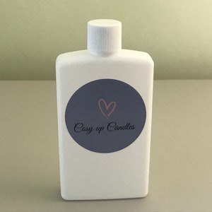 May include: A white, rectangular bottle with a white cap. A dark blue circular label features a pink heart and the words "Cosy up Candles" in cursive. The bottle is likely for a liquid product.