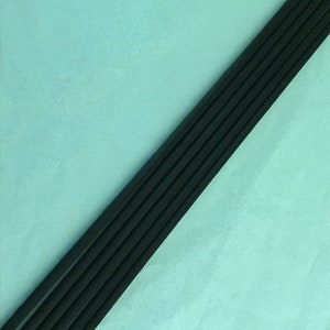 May include: A set of six black incense sticks arranged diagonally on a light blue background.