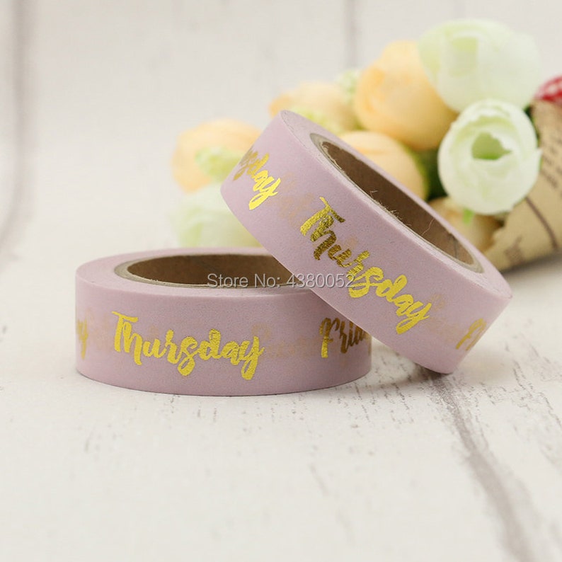May include: Two rolls of washi tape with a light purple background and gold foil lettering. The tape on the left says "Thursday" and the tape on the right says "Friday".