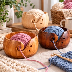 May include: Three round wooden yarn bowls with smooth finishes and spiral cutouts. One bowl holds a pink yarn ball, another a blue yarn ball, and the third a cream yarn ball. The bowls feature small circular holes for yarn guidance.
