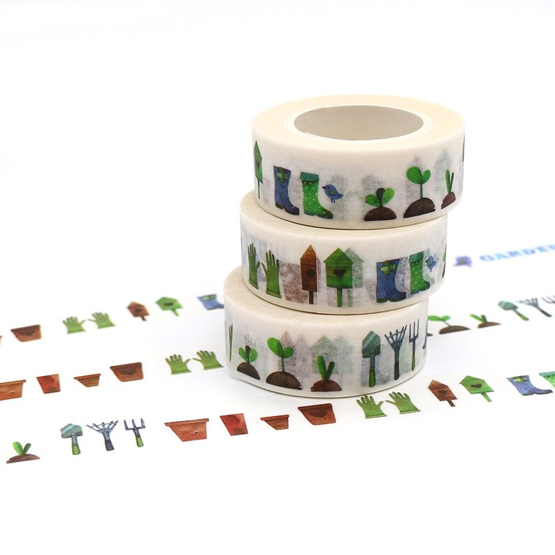 May include: Three rolls of washi tape with a gardening theme. The tape features illustrations of gardening tools, plants, and other garden-related items. The tape is white with green, blue, and brown accents.