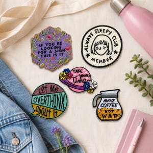 May include: Five embroidered patches featuring various designs and text: a purple hexagon with "IF YOU RE LOOKING FOR A SIGN THIS IS IT", a round "ALWAYS SLEEPY CLUB MEMBER" patch, a pink planet with "TAKE your time", a circular "Let Me OVERTHINK about it" patch, and a coffee pot with "MAKE COFFEE NOT WAR".