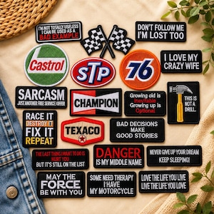 May include: A collection of embroidered patches featuring various slogans and logos, including Castrol, STP, 76, Champion, and Texaco. The rectangular, circular, and shaped patches display text like 'Don't follow me I'm lost too' and 'This is not a drill'.