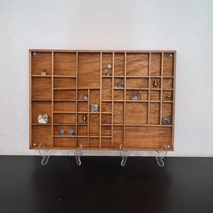 May include: A wooden display shelf with numerous small compartments, each holding a miniature object. The objects include a small car, a toy airplane, and other decorative items. The shelf is supported by clear stands.