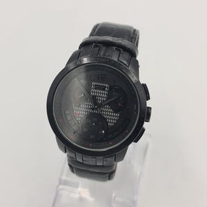 May include: A black wristwatch with a leather band. The watch face features multiple subdials and red accents. The watch is displayed on a clear stand.