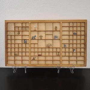 May include: A vintage wooden printer's tray with numerous small compartments, each holding miniature objects. The tray is mounted on a wall, showcasing a collection of tiny figurines, including a scale, a car, and a microphone. The overall aesthetic is nostalgic and decorative.