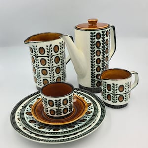 May include: A vintage ceramic coffee set with a cream-coloured coffee pot, creamer, sugar bowl, cups, and saucers. The set has a brown and green leaf and circle pattern. The plates are approximately 20 cm in diameter.