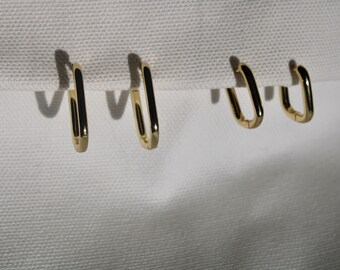 May include: Four gold hoop earrings with a rectangular shape. The earrings are hanging from a white fabric background.