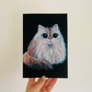 May include: A cat portrait with a black backdrop. The cat features large eyes and fluffy fur in white, orange, and brown hues. The artwork is held in a hand, showing the painting's size and detail. A charming piece of art.