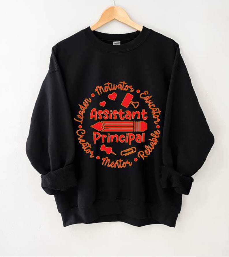 May include: Black sweatshirt with a red and orange design. The design features the words "Assistant Principal" with a pencil illustration, surrounded by words like "Leader" and "Educator". A perfect gift for school staff.