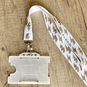 May include: White lanyard with a pink and brown leopard print lightning bolt design. The lanyard has the text "Mrs. Nicholls" printed on it. A clear plastic ID badge holder is attached to the lanyard.