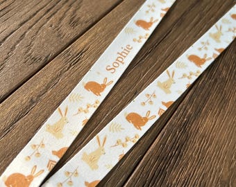 May include: A white fabric lanyard with a brown bunny rabbit pattern and the name "Sophie" printed in orange.