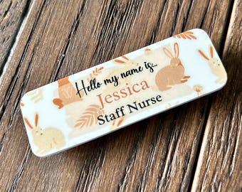 May include: White rectangular name tag with a brown bunny and floral design. The text reads "Hello my name is... Jessica Staff Nurse".