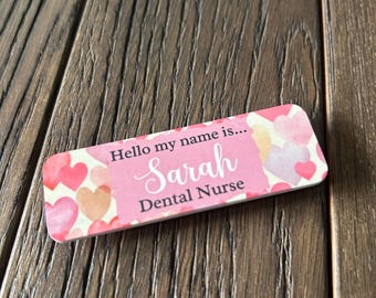 May include: Pink and white name tag with a heart pattern. The text reads "Hello my name is... Sarah Dental Nurse".