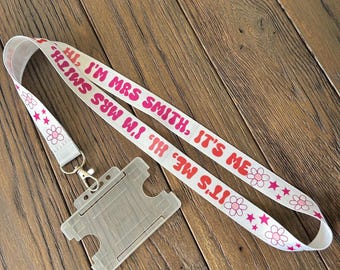 May include: White lanyard with pink and red text that reads "HI, I'M MRS SMITH, IT'S ME" and pink flowers and white stars. A clear plastic ID badge holder is attached to the lanyard.