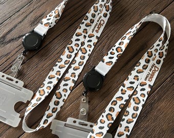 May include: Two white and brown leopard print retractable badge holders with black retractable reels. The badge holders have the names "Donna" and "Clare" printed on them.