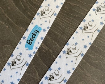 May include: White lanyard with a blue star pattern and a blue rectangle with the name "Becky" printed on it. The lanyard also features a repeated design of a person holding a bouquet of flowers.
