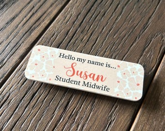 May include: White name tag with a floral pattern and the text "Hello my name is... Susan Student Midwife" in black and red.