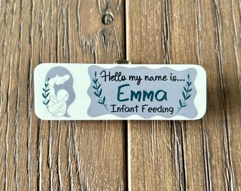 May include: White wooden name tag with a gray background and green leafy accents. The tag reads "Hello my name is... Emma Infant Feeding."