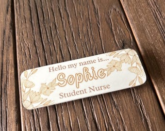 May include: A white rectangular name tag with a floral design in gold. The text "Hello my name is... Sophie Student Nurse" is printed on the tag.
