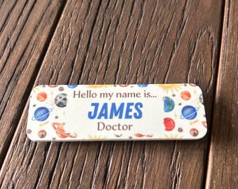 May include: A white name tag with a space theme. It says "Hello my name is... JAMES Doctor" with planets, stars, and a sun in the background.
