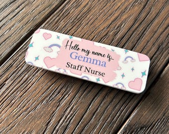 May include: A pink and white name tag with a rainbow, clouds, and hearts design. The text reads "Hello my name is... Gemma Staff Nurse".