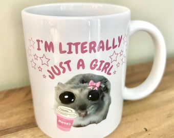 May include: White ceramic mug with a pink and black cartoon animal holding a coffee cup. The mug has the text "I'm literally just a girl" with pink stars around the text.