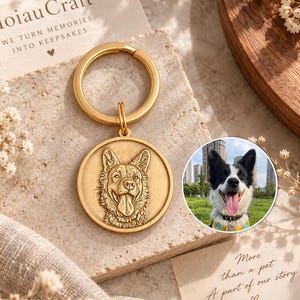 Puede incluir: Un llavero circular de metal en tono dorado con el retrato grabado de un perro con orejas puntiagudas y la boca abierta. El llavero se muestra junto a una tarjeta con el texto HoiauCraft WE TURN MEMORIES INTO KEEPSAKES y una foto circular de un perro.