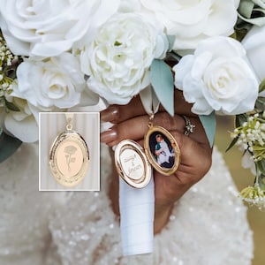 Può includere: Medaglione ovale dorato con incisione floreale e piccola foto all'interno, appeso a un nastro bianco. Il medaglione è aperto, rivelando una foto e le parole "always & forever". Il medaglione è tenuto vicino a un bouquet di rose bianche.