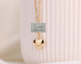 May include: Gold necklace with a heart-shaped pendant that says "love mum" on it. The necklace is on a white background.