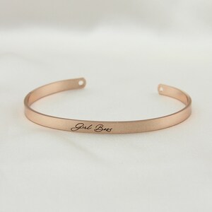 May include: A rose gold bangle bracelet with the words "Girl Boss" engraved on the front.