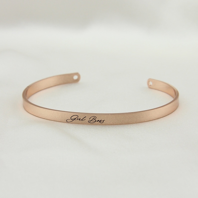 May include: A rose gold bangle bracelet with the words "Girl Boss" engraved on the front.