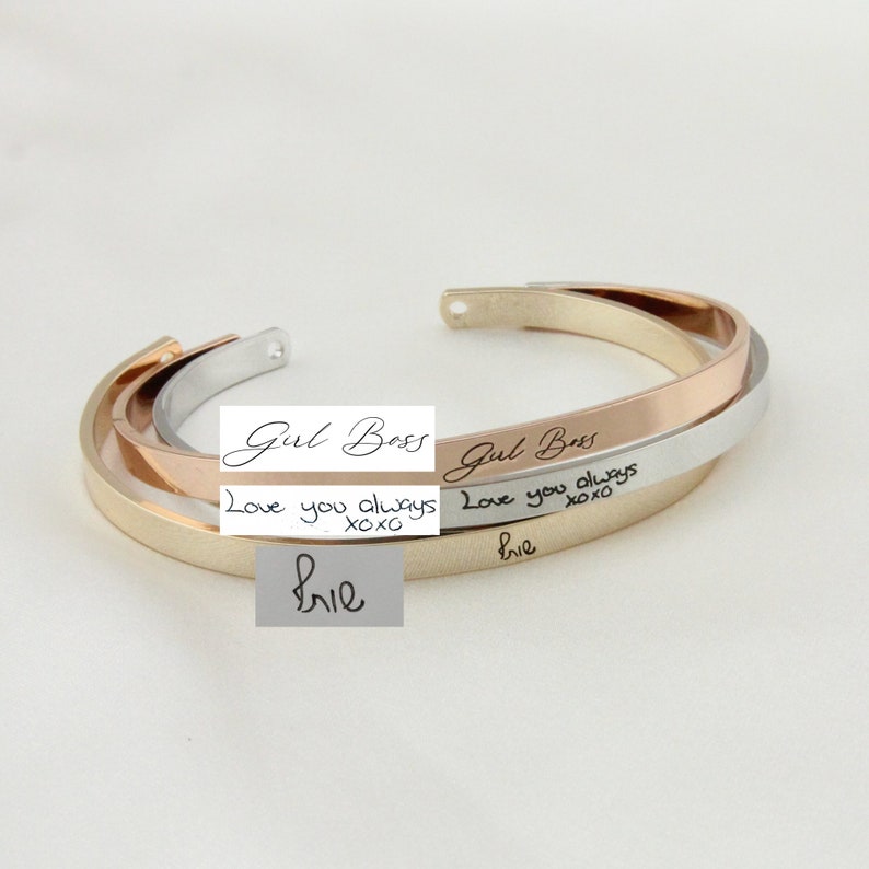 May include: Three gold, silver, and rose gold bangle bracelets with engraved text. The top bracelet reads "Girl Boss". The middle bracelet reads "Love you always xoxo". The bottom bracelet reads "Love you always xoxo" and "Brie".
