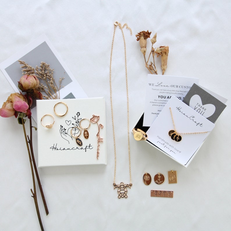 May include: A set of gold jewellery with a delicate chain necklace, a turtle pendant, and a variety of charms. The jewellery is displayed on a white surface with a small white box that says "Hoiancraft" and a card that says "We Love Our Customers".