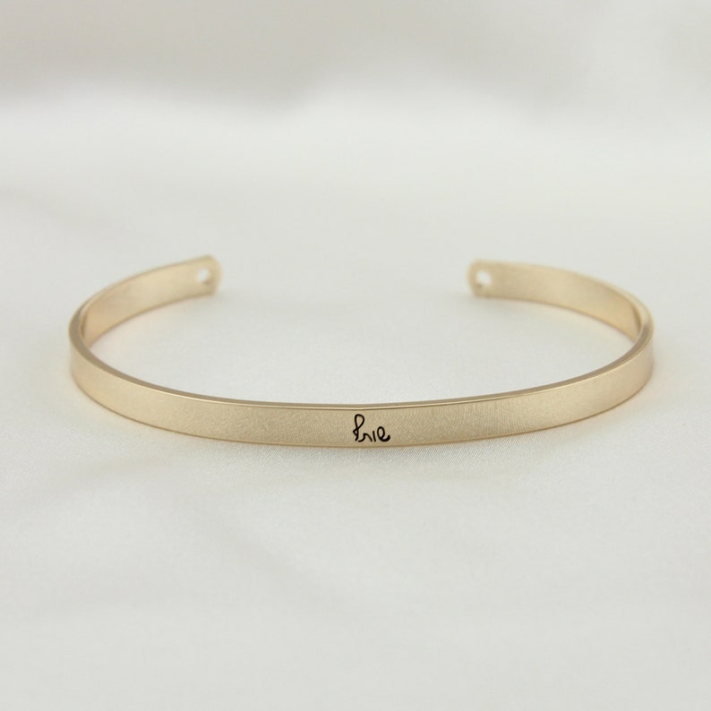 May include: A gold bangle bracelet with the word "brie" inscribed on it.