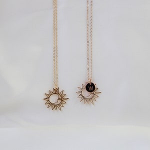 May include: Two gold necklaces with a sun and moon pendant. One pendant has a black circle with the letter W on it.