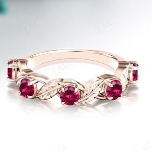 May include: Rose gold ring with a series of oval-cut, deep red gemstones set in a delicate, leaf-like design. The ring's band is smooth and polished, contrasting with the textured details of the leaves and gemstones.