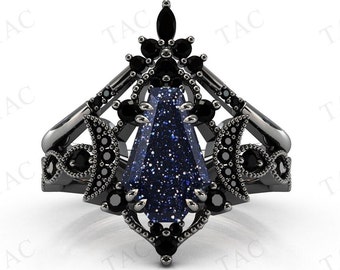 May include: A black ring set featuring a dark blue gemstone with sparkling inclusions. The ring has a unique design with black accents and smaller black gemstones. The ring is set against a white background.