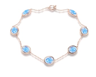May include: A delicate rose gold bracelet featuring seven oval-shaped, light blue gemstones. The gemstones are evenly spaced along the chain, creating a refined and elegant jewelry piece. The bracelet is displayed on a white background.