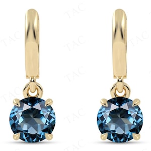 May include: A pair of gold hoop earrings with a dangling blue gemstone. The earrings are made of 14k gold and feature a round, blue topaz gemstone.