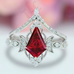 May include: A silver ring featuring a large, red, triangular gemstone surrounded by smaller diamonds. The ring has a delicate, intricate design with a crown-like top.