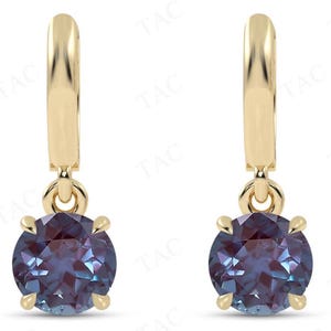May include: A pair of gold hoop earrings with a dangling round alexandrite gemstone. The earrings are a classic style and would make a great gift.