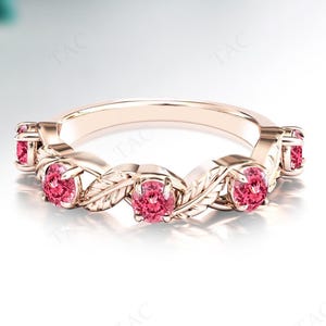May include: Rose gold ring featuring a leaf design with oval-cut pink gemstones. The ring has a delicate, nature-inspired aesthetic. The gemstones are set in a repeating pattern around the band, creating a continuous sparkle.