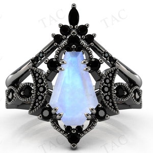 May include: A black ring with a large, pear-shaped moonstone set in a delicate, intricate design. The ring is adorned with smaller black gemstones.