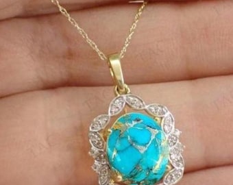 May include: Gold-tone necklace with a pendant featuring a vibrant turquoise stone with gold veining, set in a diamond-accented floral frame. The pendant hangs from a delicate gold chain, creating an elegant jewelry piece.
