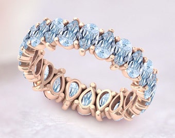 May include: A rose gold eternity band with a row of pear-shaped aquamarine gemstones.