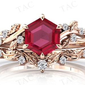 May include: A rose gold engagement ring set with a large red ruby gemstone in a hexagonal cut. The ring features a delicate floral design with small diamonds.
